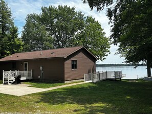 A small cabin with a porch and a dock extending into a lake, surrounded by trees. - Lakefront Cottage on South Manistique Lake (curtis)