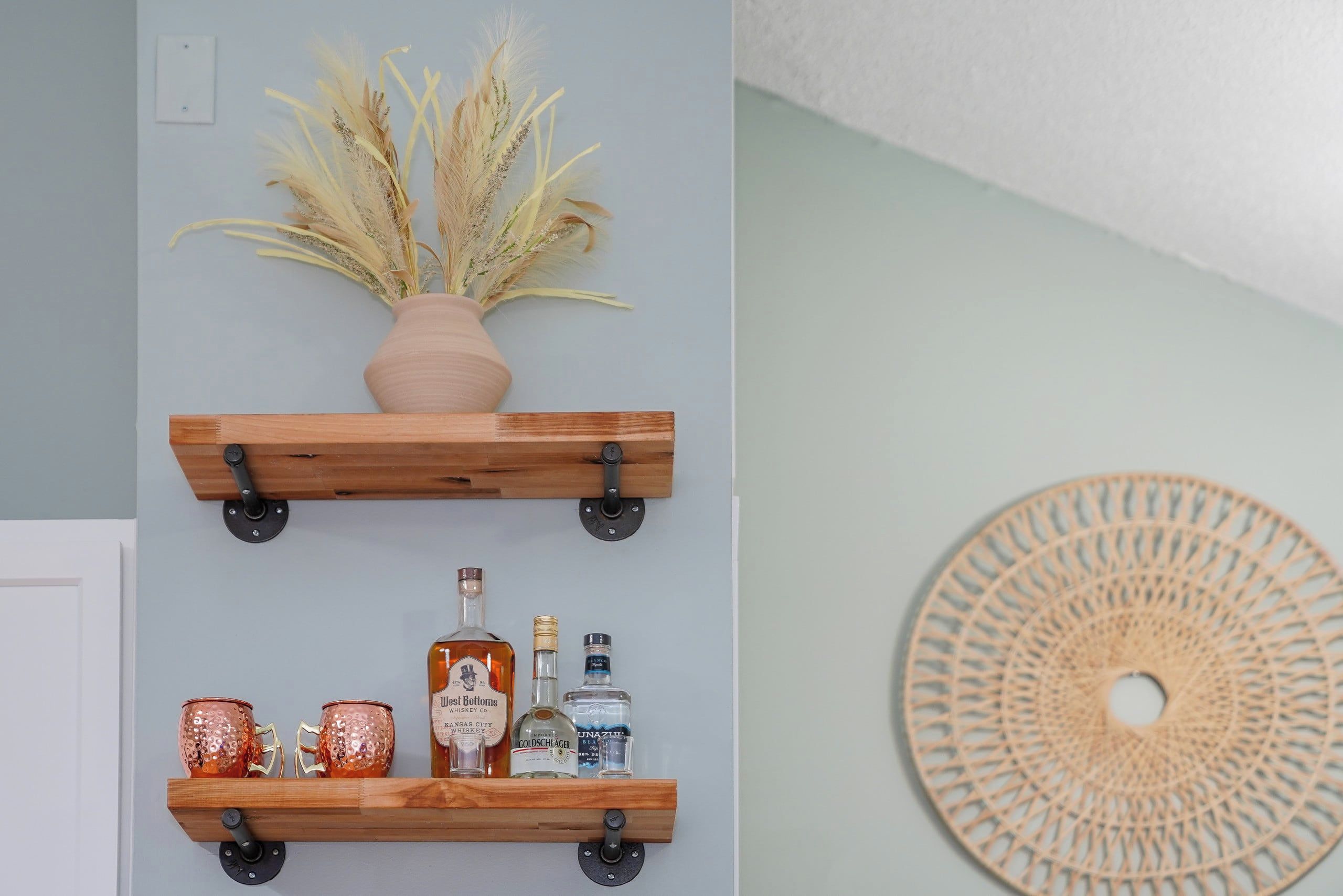 Two wooden shelves with a vase of dried plants and bottles of liquor.