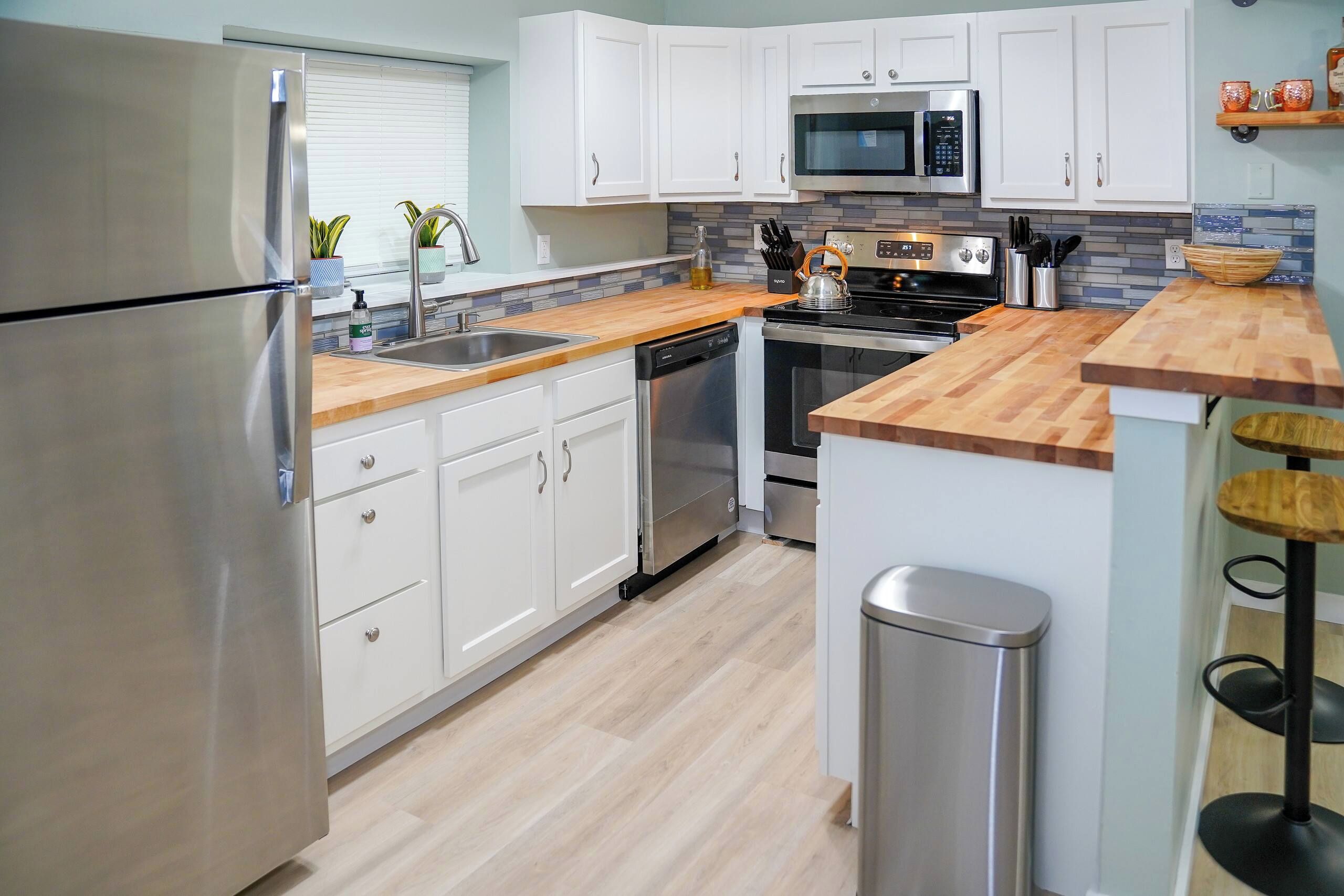 A modern kitchen with stainless steel appliances, white cabinetry, and a wooden countertop.