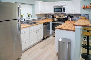 Une cuisine moderne dotée d’appareils électroménagers en acier inoxydable, de meubles de rangement blancs et d’un plan de travail en bois.