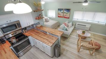 A modern kitchen with a wooden countertop, stainless steel appliances, and a dining area with a wicker chair and a round table.