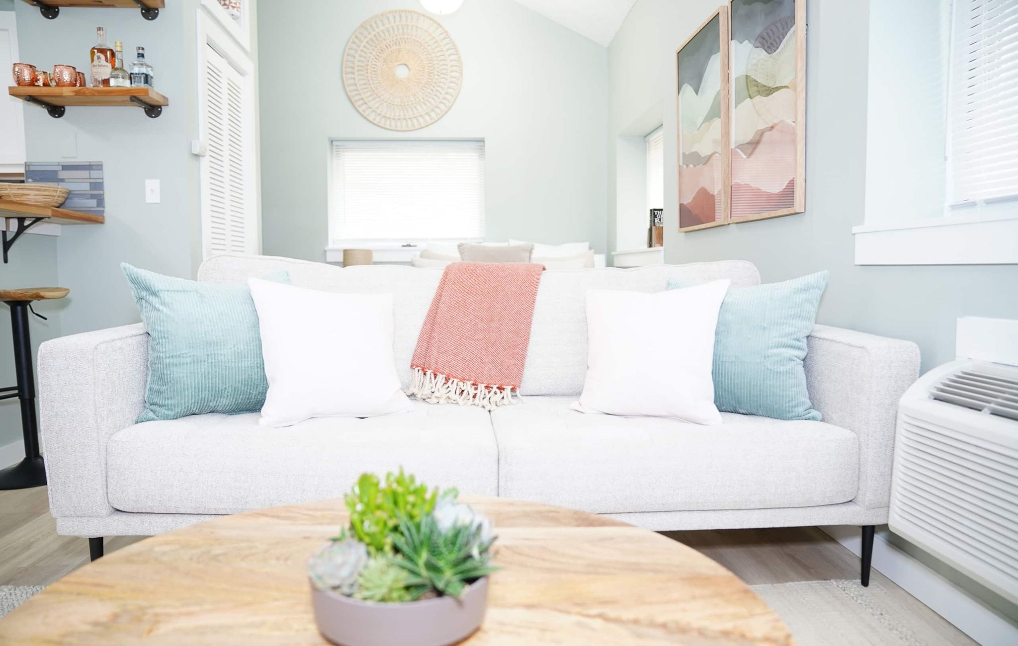 A modern living room with a white sofa, a round coffee table with a plant, and a wall-mounted circular light fixture.