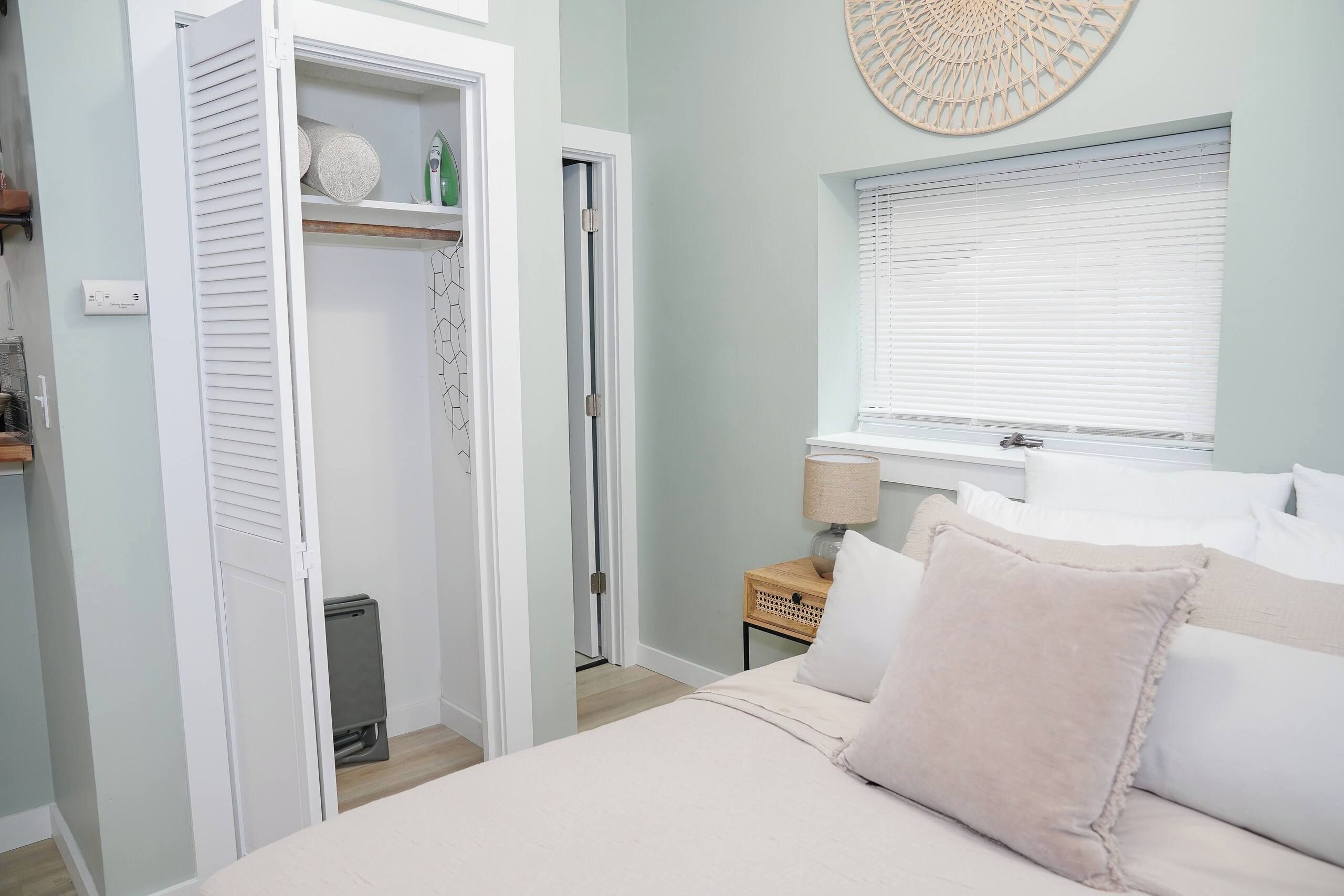 Une chambre à coucher comprenant un lit, une table de chevet avec une lampe, une fenêtre avec des stores et une armoire avec une tringle à vêtements.