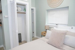 Une chambre à coucher comprenant un lit, une table de chevet avec une lampe, une fenêtre avec des stores et une armoire avec une tringle à vêtements.