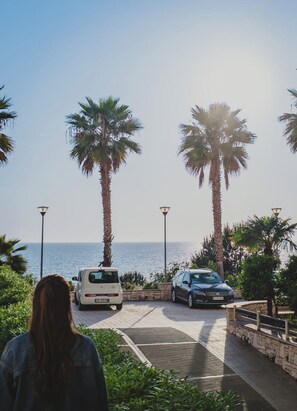 Ein Parkplatz mit zwei Autos, Palmen und Blick auf das Meer.