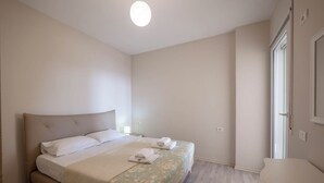 A bedroom with a bed, a bedside table, a window, and a door. - Albania Dream Beachfront Apartment (Sarand)