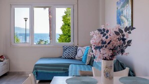 A room with a bed, a dining table with placemats, a vase with flowers, and a painting on the wall. - Albania Dream Beachfront Apartment (Sarand)