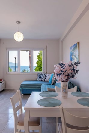 A room with a bed, a dining table with placemats, a vase with flowers, and a painting on the wall.