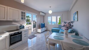 A modern kitchen with a microwave, oven, and dining area with a table and chairs. - Albania Dream Beachfront Apartment (Sarand)