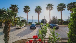 A parking area with three cars, palm trees, and a view of the sea. - Albania Dream Beachfront Apartment (Sarand)