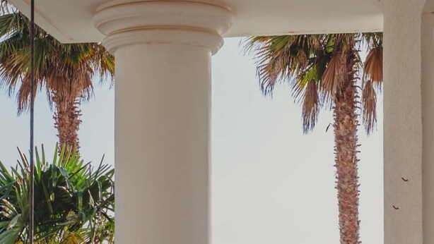 A balcony with a view of the sea, palm trees, and a car parked outside. - Albania Dream Beachfront Apartment (Sarand)
