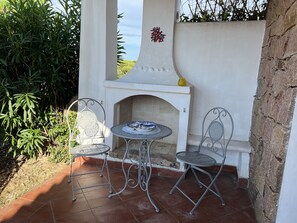 Eine Terrasse im Freien mit zwei Metallstühlen und einem kleinen Tisch, eine weiße Wand mit einer Dekoration sowie eine Steinwand.