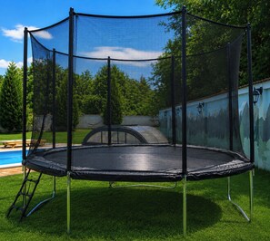 A trampoline with a safety net enclosure in a grassy backyard. - Avrigelli, kids&family friendly (Avrig)