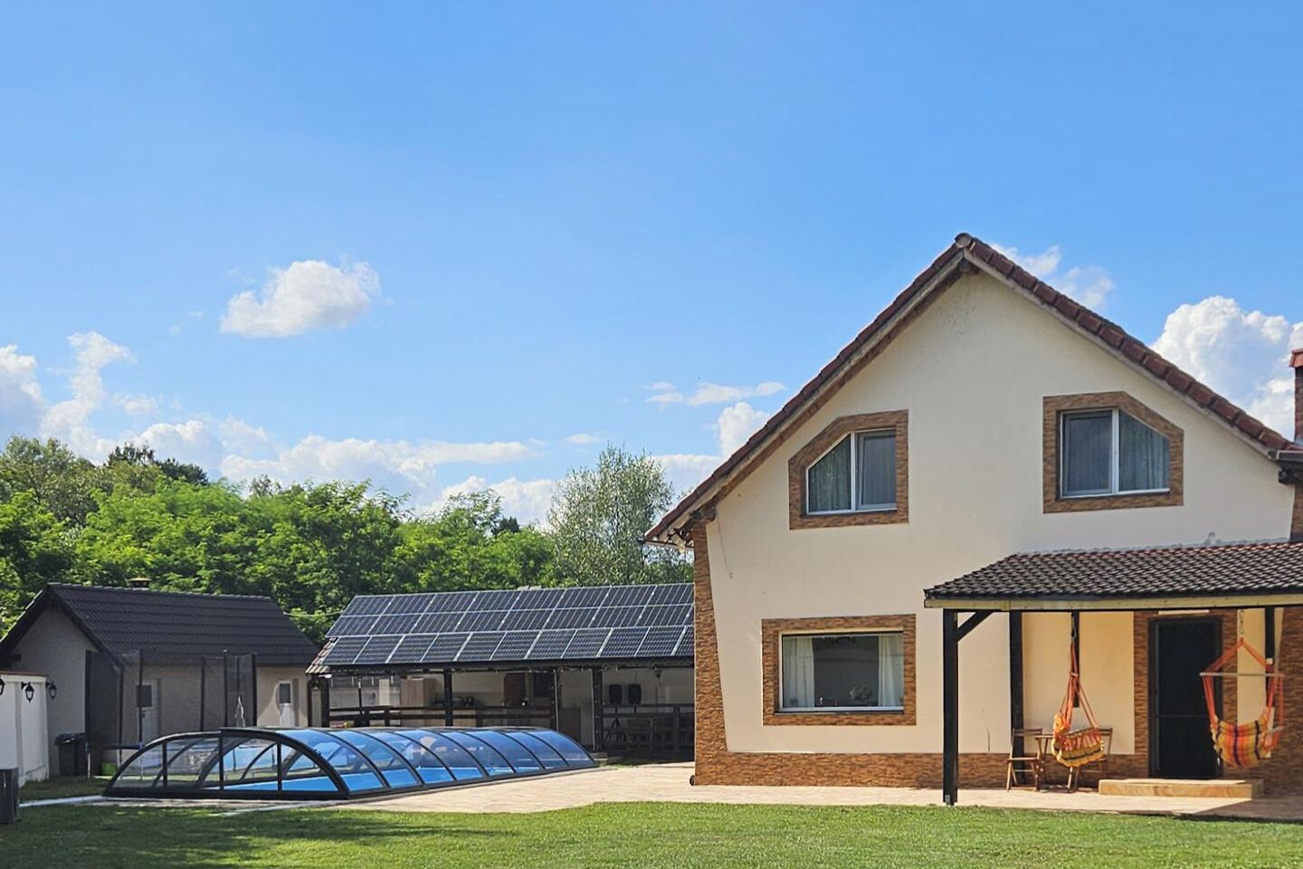 A house with a solar panel roof, a covered swimming pool, and a patio with outdoor furniture.