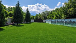 A well-maintained grassy area with a hammock, trees, and a mural on a building wall. - Avrigelli, kids&family friendly (Avrig)