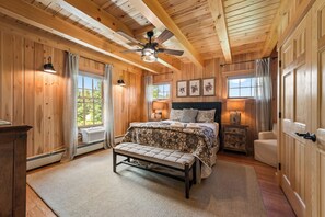 A wooden cabin bedroom with a bed, bench, bedside tables, and a ceiling fan.