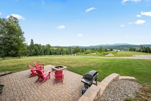 A patio with red Adirondack chairs, a fire pit, and a grill.