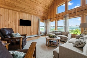 Una sala de estar acogedora con paredes de madera, un televisor de pantalla plana, un sillón de cuero, un sofá y una mesa de centro con juegos de mesa.