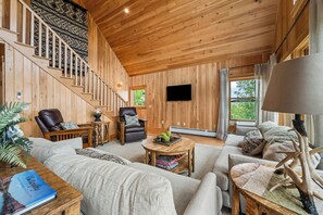 Um interior em madeira com uma escada, uma televisão de tela plana e um sofá.