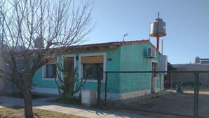 Un petit bâtiment avec un réservoir d’eau sur le toit, une cour clôturée et un arbre devant.