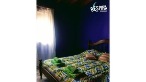 Une chambre à coucher avec une couvre-lit à motifs floraux, une tête de lit en bois et une fenêtre ornée de rideaux légers.
