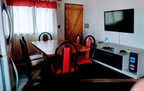 A dining area with a wooden table and red upholstered chairs, a television mounted on the wall, and a wooden door.