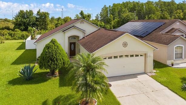 Une maison de plain-pied avec un garage, des panneaux solaires et une pelouse bien entretenue.