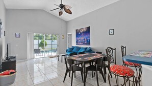 Un salon spacieux doté d’un ventilateur de plafond, d’un canapé bleu, d’une table à manger avec des chaises et d’une grande fenêtre donnant sur l’extérieur.