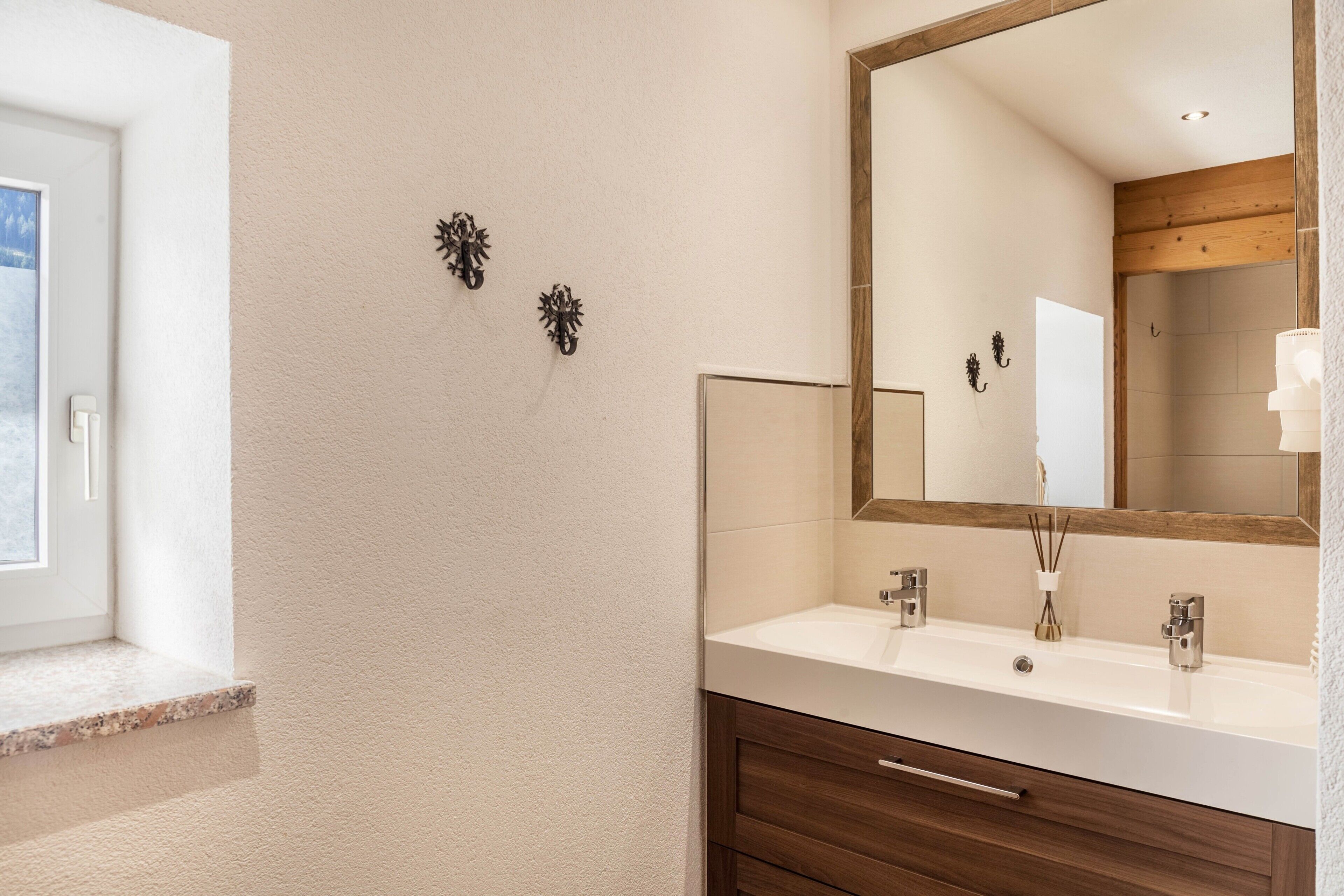 A bathroom with a large mirror, two wall-mounted sconces, a wooden vanity, and a window.