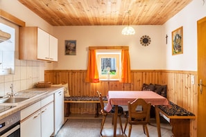 A compact kitchen with wooden cabinets, a sink, and a window with orange curtains. - Neuhaus Alm Holiday Home with Mountain Views, Open Terrace and Wi-Fi (Gerlosberg)