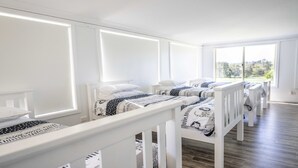 Una stanza luminosa e spaziosa con pareti bianche e ampie finestre, con tre letti dotati di ringhiere bianche e biancheria da letto decorata.