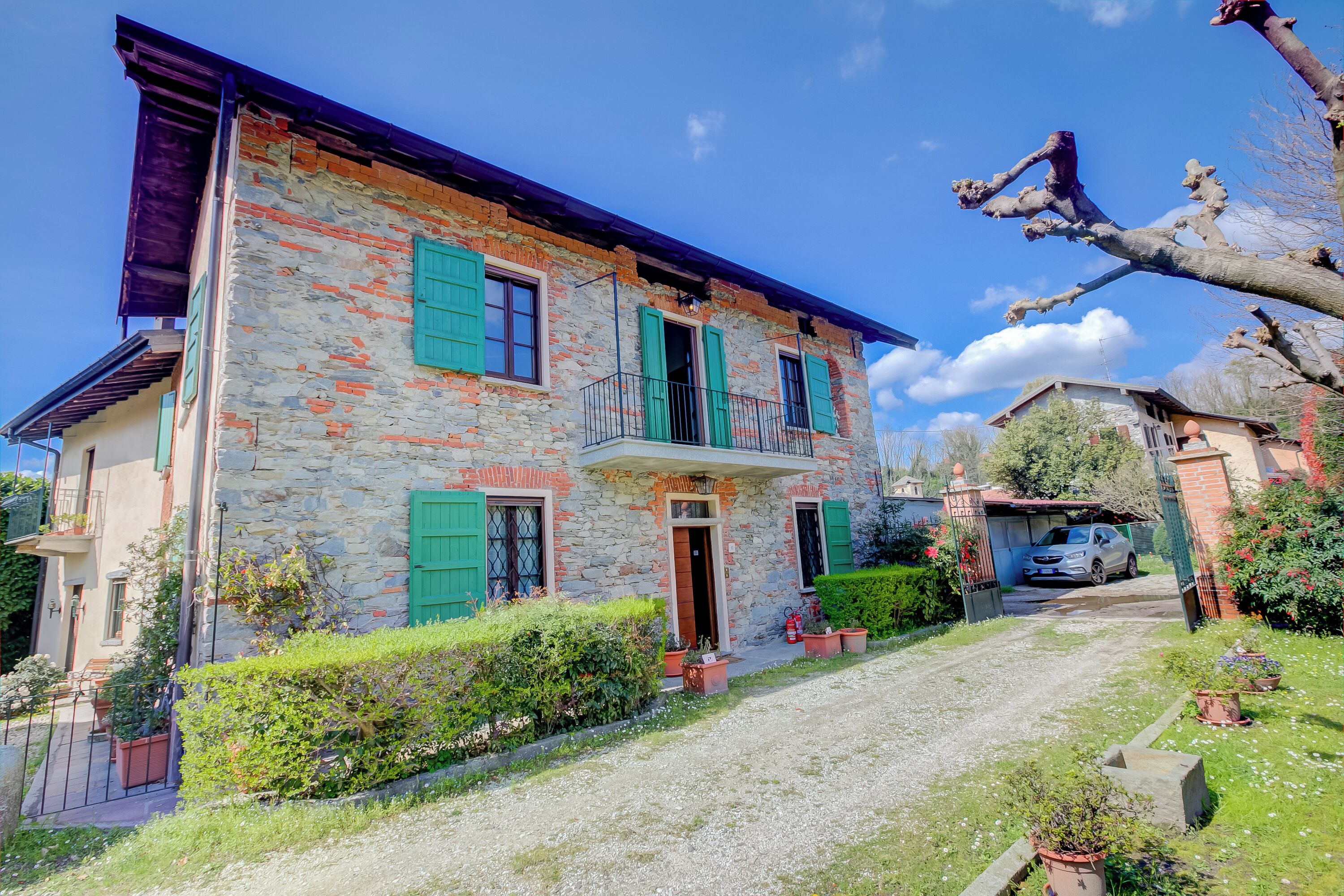 Un edificio de piedra con contraventanas verdes, un balcón y un camino de grava.