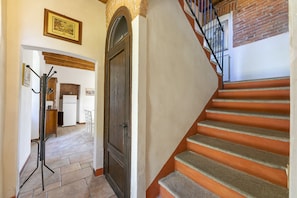 Eine Treppe mit orangefarbenen Stufen führt zu einer Zwischenebene, einem Holztür und einem Flur mit Fliesenboden.