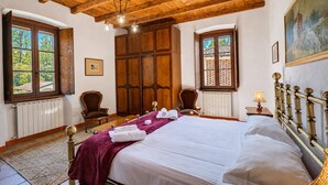 A bedroom with a wooden ceiling, a large bed, two chairs, a wooden wardrobe, and a window with a view of trees. - Timeless l'Antico Mulino Della Bozza in Brebbia, Brebbia, Italy (Brebbia)