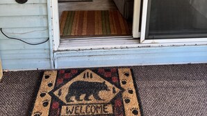 A cozy living room with a sofa, ottoman, and a rug. - The Bears Den cabin w screened porch in campground on bike trail. (Boulder Junction)