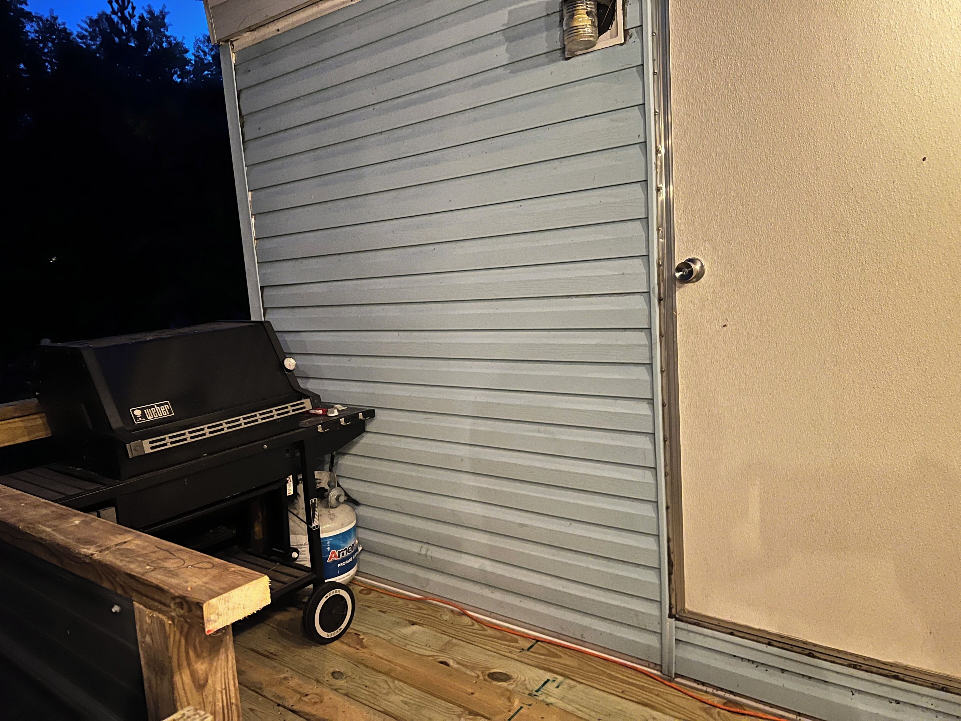Un barbecue avec une bouteille de propane sur une terrasse en bois.
