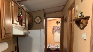 A narrow hallway with wooden cabinets, a white refrigerator, and a gas stove. - The Bears Den cabin w screened porch in campground on bike trail. (Boulder Junction)