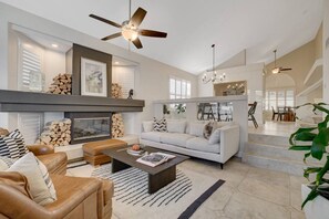 Ein geräumiges Wohnzimmer mit Kamin, einer Couch, einem Couchtisch und einem Deckenventilator.