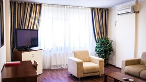 A living room with a television, two armchairs, a coffee table, a small table with a book, and a potted plant. - Europa Residence (Atyrau)