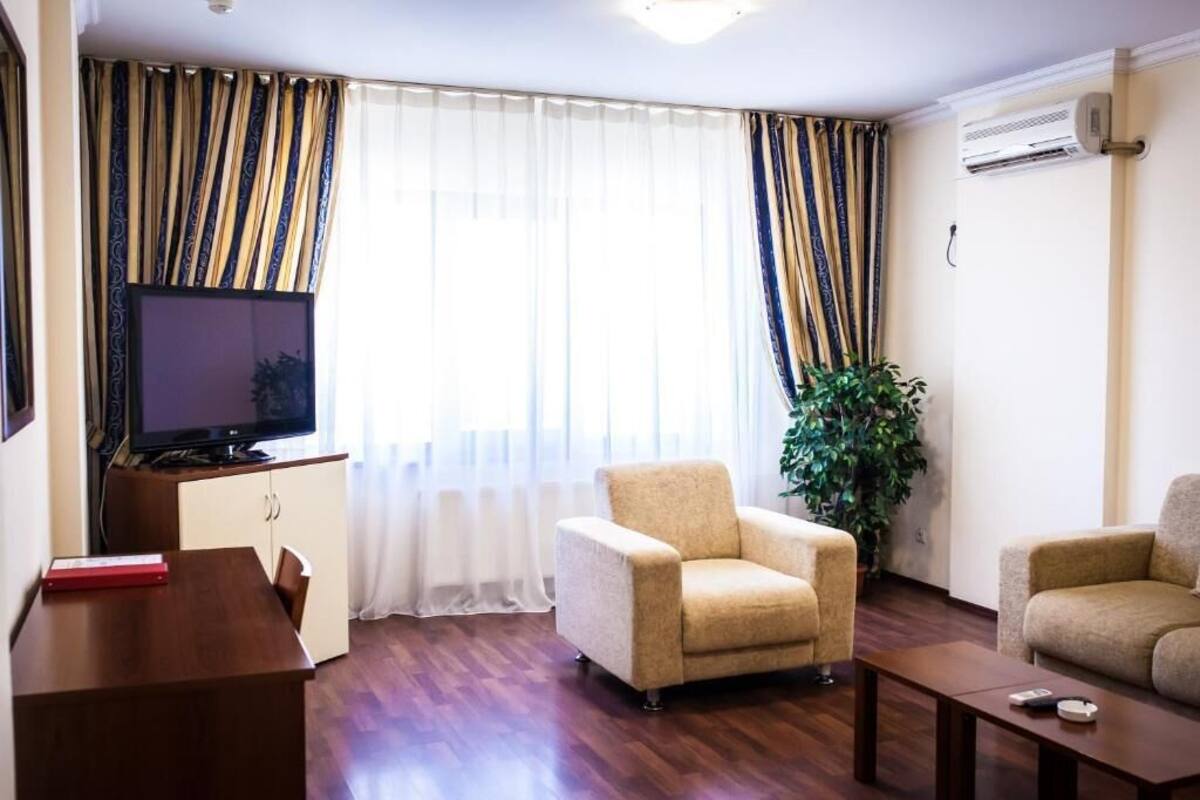 Una sala de estar con televisor, dos sillones, una mesa de centro, una mesita con un libro y una planta en maceta.
