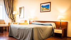 A hotel room with a large bed, two bedside tables with lamps, a chair, and a painting on the wall. - Europa Residence (Atyrau)