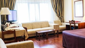 A hotel room with a sofa, a bed, a desk, and a television. - Europa Residence (Atyrau)