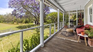 Eine überdachte Veranda mit Holzterrasse, einem roten Sofa und einem Grill.