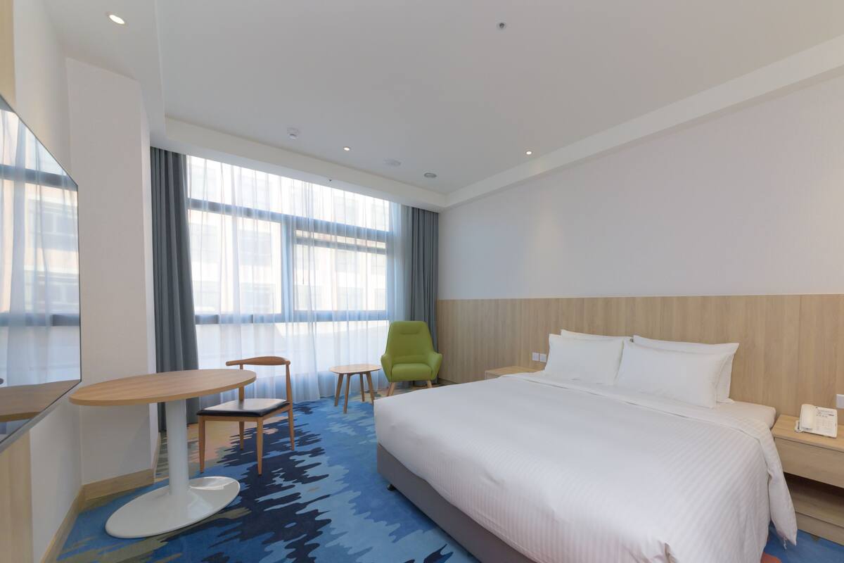 A hotel room with a large bed, a desk, a chair, and a small table.