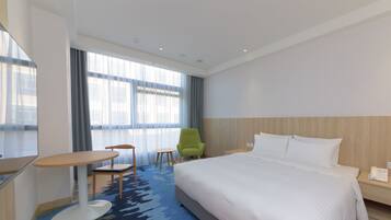 Quarto de hotel com uma cama grande, uma escrivaninha, uma cadeira e uma pequena mesa.