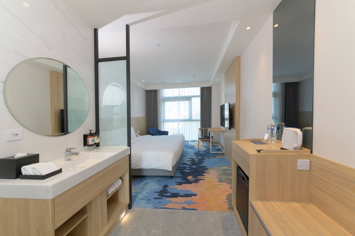 A hotel room with a large bed, a sitting area with a table and chairs, a bathroom with a sink and mirror, and a TV.