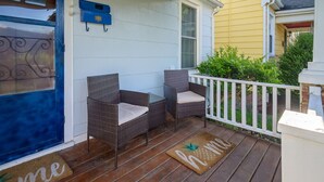 Una terraza de madera con dos sillas de mimbre y un felpudo con la palabra 'home'.