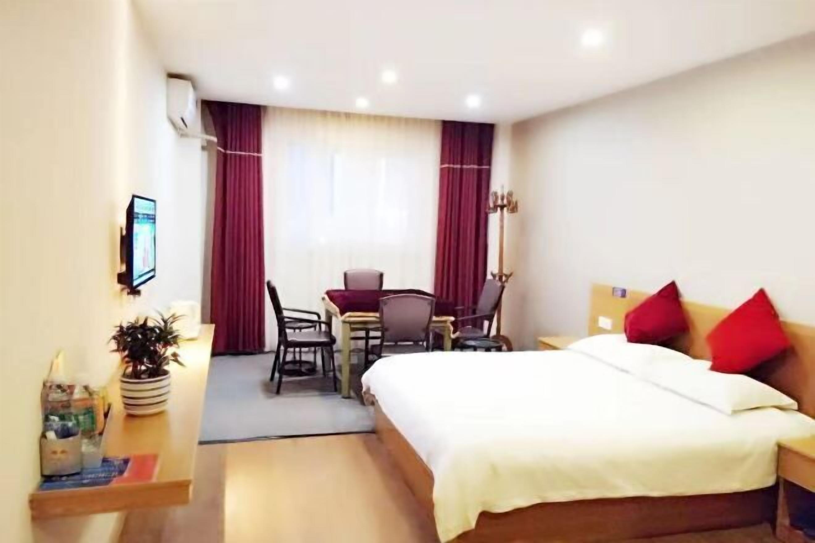 A hotel room with a bed, a desk, a chair, a TV, and a window with curtains.