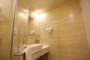 A bathroom with a glass shower enclosure, a sink with a towel, and a hand dryer mounted on the wall.