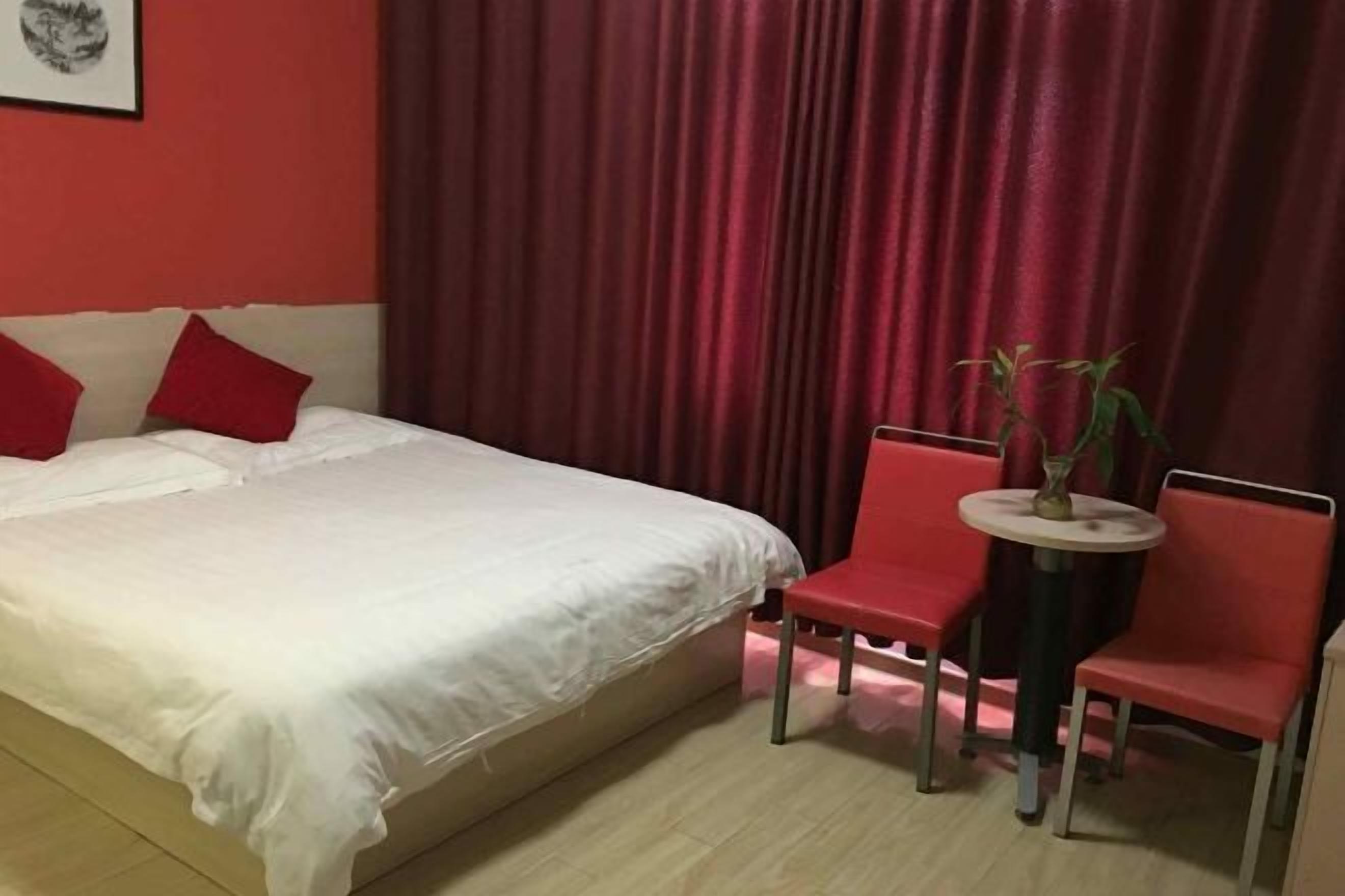 Une chambre à coucher avec un lit, deux chaises rouges, une petite table et un rideau.